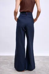 Pantalon de vestir de corte recto y tiro alto, confeccionado en tela de lino en color beige. Presenta pinzas frontales, cierre con botón y detalle de vivos en contraste en la cintura.