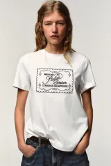 Camiseta blanca de manga corta y cuello redondo, con aplicación de organza y texto negro a contraste en el pecho.