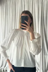 Camisa negra de manga larga con cuello alto tipo victoriano y detalle de fruncido en el pecho y puños. Presenta cierre frontal con botones y diseño de mangas abullonadas.