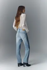 Jean de tiro alto confeccionado en denim azul rígido con lavado claro localizado y efecto de bigotes. Presenta un corte de pierna recta y apliques laterales de tachas brillantes.