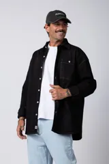 Camisa de manga larga estilo sobrecamisa, color negro, con corte oversize, cuello clásico, cierre frontal con botones y bolsillo frontal en el pecho.