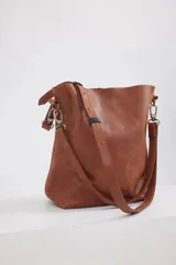 Cartera tipo shopper de cuero color suela, con diseño minimalista, correa larga ajustable y herrajes metálicos en tono bronce.