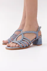 Sandalia de mujer color celeste, con tiras trenzadas en el empeine y pulsera ajustable con hebilla. Posee taco ancho y bajo, y suela de color marrón claro.