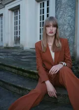 Chaqueta color marrón con cuello de solapa, manga larga con puños abotonados, dos bolsillos frontales de parche, un bolsillo de parche en el pecho, abertura posterior en el bajo y forro interior.