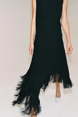 Vestido midi de Zara Woman Collection color negro, sin mangas, con cuello redondo y espalda abierta. Presenta un diseño asimétrico en el bajo adornado con flecos a tono, y cierre trasero con cremallera y botón.