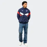Buzo tipo rompevientos de nylon con medio cierre frontal, cuello alto y puños elásticos. Presenta un diseño en bloques de color azul, blanco y bordó, con el escudo del Club Nacional de Football y el logo de Umbro estampados en el pecho.