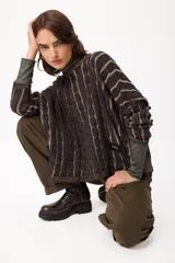 Sweater de punto con diseño de trenzas verticales en color negro y marrón, de corte holgado y cuello redondo. Presenta mangas largas y una etiqueta decorativa en el lateral inferior.