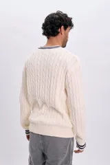 Sweater tejido de punto color crudo, con diseño trenzado y detalles de líneas azul marino en el cuello redondo y los puños.