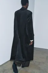 Abrigo largo de Zara confeccionado en tejido de pana con textura acanalada. Presenta un diseño de corte recto, cuello con solapas, cierre frontal cruzado con botones y bolsillos delanteros. Incluye forro interior a tono.