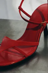 Sandalia de piel color rojo con diseño de tiras finas en la parte delantera. Cuenta con cierre de pulsera al tobillo mediante hebilla metálica y tacón de altura media en color negro.