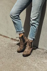 Bota tipo chelsea de cuero rústico color marrón, con paneles elásticos laterales y detalles de perforaciones estilo brogue. Cuenta con suela de goma resistente y tiradores en la parte superior de la caña.