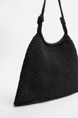 Bolso tipo shopper color crudo, confeccionado en tejido trenzado de algodón con diseño de macramé. Cuenta con dos asas de hombro ajustables que funcionan como cierre del compartimento principal.