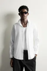 Camisa de vestir blanca de corte slim fit, confeccionada en tejido de algodón con textura estructurada. Cuenta con cuello italiano, mangas largas con puños abotonados y cierre frontal con botonadura.