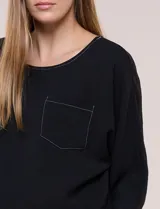 Blusa oversize color negro con caída fluida, escote redondo, bolsillo frontal en el pecho, mangas tres cuartos de hombro caído y costuras a la vista en contraste.