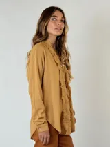 Camisa color mostaza con volados desflecados a lo largo de la botonadura frontal, cuello mao y mangas largas con puños abotonados.