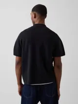 Buzo tipo polo de manga corta color gris oscuro, tejido de punto, con cierre frontal parcial en el cuello y un bolsillo aplicado en el pecho.