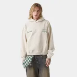Hoodie de corte oversized color beige con capucha y bolsillo frontal tipo canguro. Presenta estampados gráficos circulares en color verde en la espalda con tipografía y logos de la marca.