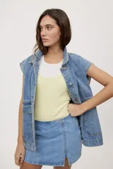 Chaleco de jean azul de calce relajado, con cuello camisero, cierre frontal con botones metálicos y bolsillos delanteros grandes con solapa.