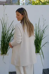 Saco abierto tipo cárdigan color crudo, de corte recto y largo medio, con mangas largas y dos bolsillos frontales aplicados.