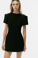 Vestido mini negro con cuello redondo, manga corta con pliegues y costuras marcadas. Cuenta con cierre posterior con cremallera oculta.