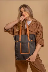 Bolso tipo tote bag de símil cuero color rosa pálido, con asas dobles y detalles de costura en color beige claro. Presenta un bolsillo frontal rectangular aplicado y herrajes metálicos.