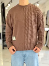 Sweater de punto oversize color marrón, con cuello redondo y diseño combinado: la mitad derecha cuenta con tejido de ochos y la izquierda es lisa. Incluye una etiqueta decorativa blanca en el frente inferior derecho.