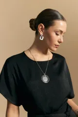 Top negro de manga corta con silueta amplia y caída fluida, confeccionado en un tejido liviano con leve brillo. Presenta un botón de nácar en la espalda con una pequeña abertura y mangas amplias tipo kimono.