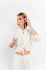 Blusa corta de lino color blanco, con mangas largas abullonadas, cuello alto con volados y cierre frontal con tiras para anudar. Presenta detalles de encaje en los bordes.