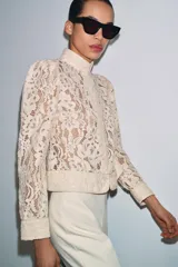 Blazer de encaje con cuello redondo, manga larga con puños y cierre frontal con botones. Presenta un diseño estructurado con bajo recto.