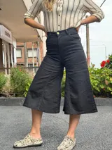 Jean capri negro de tiro alto con diseño de pierna amplia tipo culotte, confeccionado en denim con lycra, bolsillos y botón frontal.