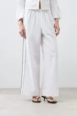 Pantalón de lino blanco de corte palazzo, con cintura elastizada y cordón ajustable. Presenta un vivo negro en el lateral.