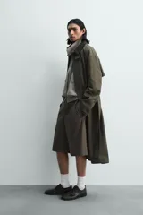 Bermuda de vestir color marrón oscuro, corte relajado y tiro alto, con pliegues frontales y cierre de botón y cremallera.