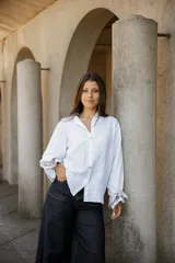 Camisa de lino blanca con cuello camisero, cierre frontal de botones de nácar y mangas largas con puños en contraste de tela rayada.