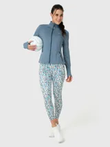 Campera deportiva de ajuste entallado, confeccionada en tejido técnico suave de color azul melange. Presenta cuello alto con cierre frontal, mangas largas con orificio para pulgar y bolsillos laterales con cierre.
