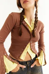 Top de manga larga color amarillo, confeccionado en tejido acanalado con cierre frontal de botones a presión metálicos. Presenta detalles de botones en los puños y un corte ajustado al cuerpo.