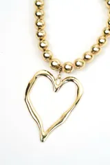Collar dorado compuesto por cuentas esféricas metálicas y un gran dije colgante en forma de corazón con diseño orgánico y textura irregular.