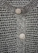 Chaqueta de punto con acabado brillante de lúrex, cuello redondo y cierre frontal con botones joya. Presenta un diseño recto de manga larga.