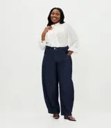 Pantalón de jean raw azul oscuro, corte barrel con piernas anchas y cintura cónica. Presenta costuras contrastantes, cierre tradicional con botón y bolsillos laterales.