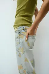 Jeans de tiro bajo y corte holgado, color celeste con estampado floral en tonos amarillos y verdes. Presenta diseño de cinco bolsillos, trabillas para cinturón y dobladillo con vuelta en los bajos. Cierre frontal con cremallera y botón metálico.