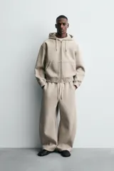 Sudadera tipo hoodie con cierre frontal de cremallera, confeccionada en tejido técnico de algodón con efecto neopreno. Presenta un corte relajado, capucha ajustable con cordones, bolsillos frontales tipo canguro y terminaciones con elástico en puños y ruedo.