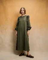 Vestido midi de corte holgado en color verde oliva, con mangas largas abullonadas que presentan detalles de volados en los hombros y puños elásticos.