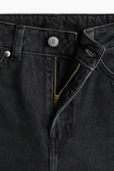 Jean de tiro alto y estilo baggy color negro, confeccionado en denim de algodón rígido, con diseño de cinco bolsillos, cierre de cremallera y botón metálico, y perneras amplias de corte holgado.