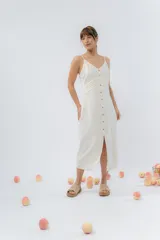 Vestido midi color crudo, de breteles finos regulables, con botones de madera en el frente y pliegues decorativos en la cintura. Tiene cierre invisible en el costado.