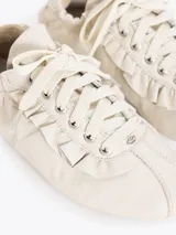 Zapatillas urbanas de cuero vacuno en color beige, con detalles de volados en los laterales de los cordones y suela de goma plana con textura.