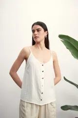 Musculosa color blanco roto con escote en V y botones frontales. La tela presenta una textura arrugada o plisada.