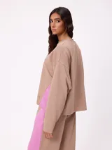 Sweater de corte oversize y estilo cropped, color gris oscuro, con cuello redondo y detalle de costura en forma de X en el pecho. Presenta un pequeño logo bordado en el ruedo inferior.