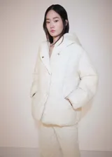 Campera puffer de corte oversize y diseño recto, color blanco crema. Cuenta con capucha, cuello alto, cierre frontal con botones y dos bolsillos laterales. Confeccionada en tejido de nylon con relleno acolchado.