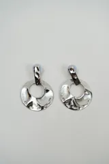 Aros colgantes de diseño circular con acabado plateado y textura irregular. Presentan un detalle superior rectangular y perforaciones decorativas en el borde inferior.