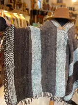 Poncho de lana virgen tejido en telar con diseño de rayas verticales en tonos marrón y celeste, con terminación de flecos en los bordes y cuello en V con detalle de refuerzo en cuerina.