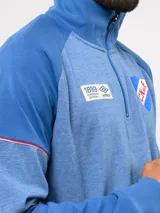 Buzo deportivo de medio cierre marca Umbro del Club Nacional de Football. Presenta un diseño en tonos azul y gris jaspeado, con cuello alto, mangas largas y detalles de costuras en contraste. Incluye el escudo del club y logo de la marca en el pecho.